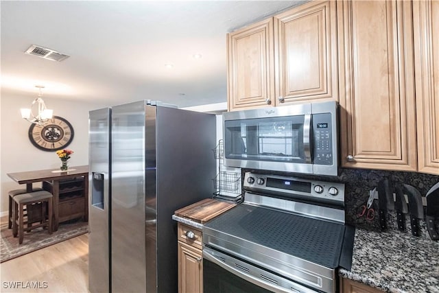 kitchen with appliances with stainless steel finishes, tasteful backsplash, light wood-type flooring, dark stone countertops, and a chandelier