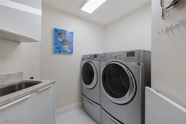 washroom with light tile patterned floors, a sink, washing machine and clothes dryer, and baseboards