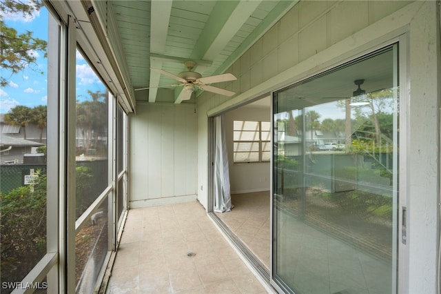 unfurnished sunroom featuring beamed ceiling, ceiling fan, and a wealth of natural light