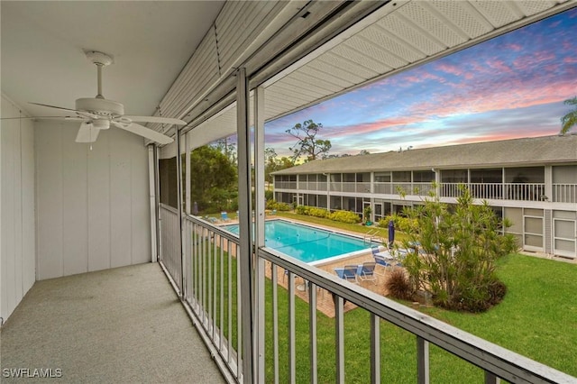 pool at dusk with a yard and ceiling fan