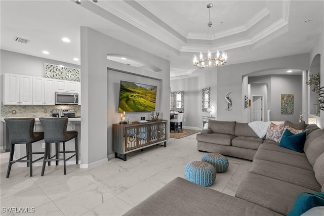 living room with a tray ceiling, ornamental molding, and a notable chandelier