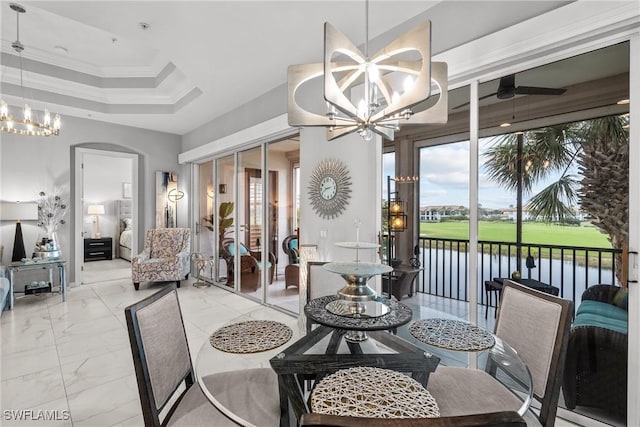 dining room featuring ceiling fan with notable chandelier, ornamental molding, a water view, and a raised ceiling