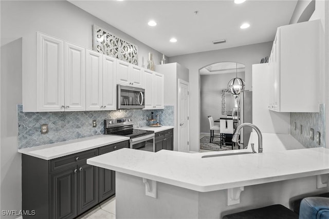 kitchen featuring kitchen peninsula, a breakfast bar area, appliances with stainless steel finishes, pendant lighting, and white cabinets