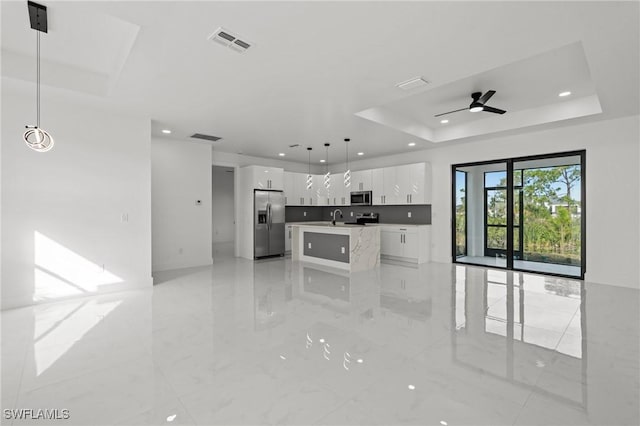 kitchen featuring pendant lighting, white cabinetry, a kitchen island with sink, stainless steel appliances, and a tray ceiling