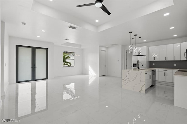 kitchen featuring pendant lighting, appliances with stainless steel finishes, white cabinetry, light stone counters, and a raised ceiling