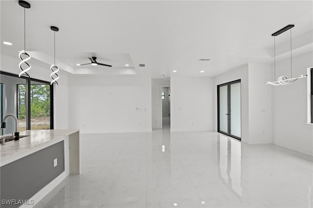 kitchen featuring light stone counters, sink, decorative light fixtures, and a raised ceiling