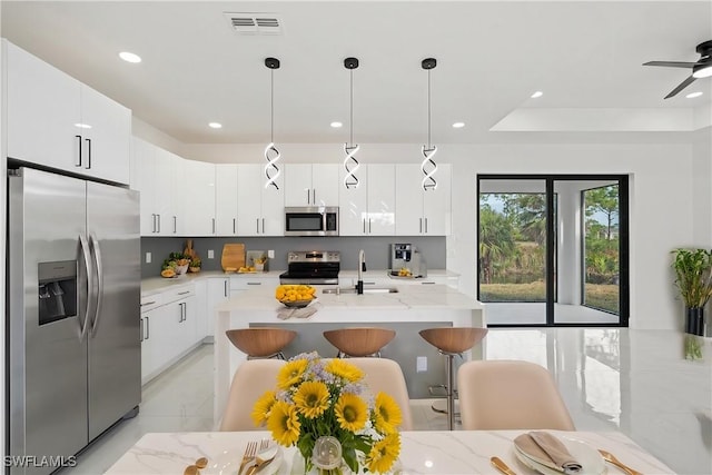 kitchen featuring a breakfast bar, decorative light fixtures, white cabinetry, sink, and stainless steel appliances