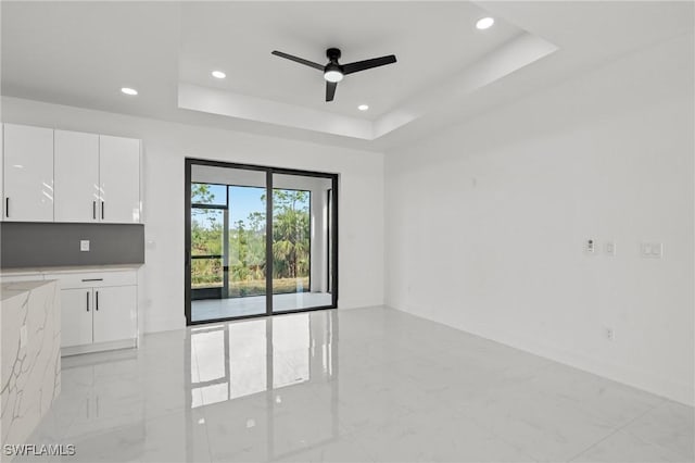 unfurnished living room featuring a raised ceiling and ceiling fan