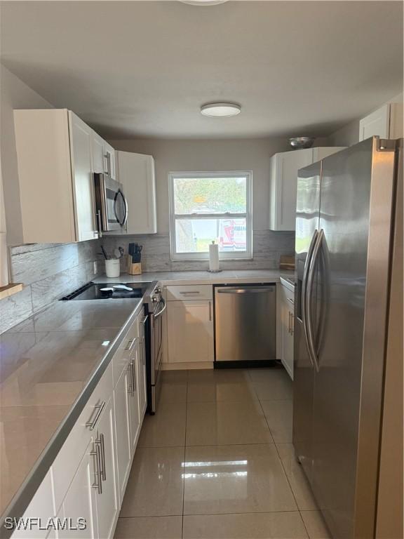 kitchen with tasteful backsplash, white cabinets, light tile patterned floors, and stainless steel appliances