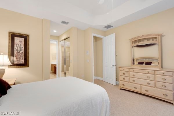 bedroom with ceiling fan, ensuite bathroom, light colored carpet, and a closet