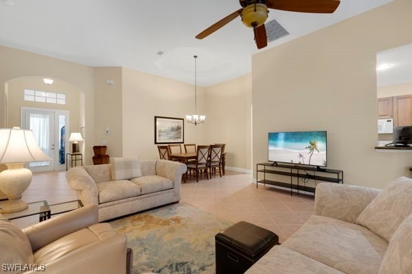 tiled living room with ceiling fan with notable chandelier and french doors