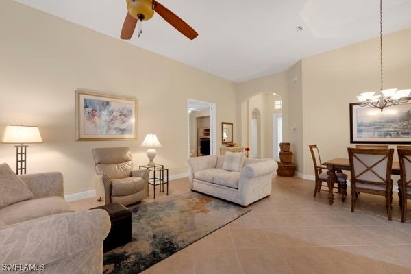 tiled living room with ceiling fan with notable chandelier