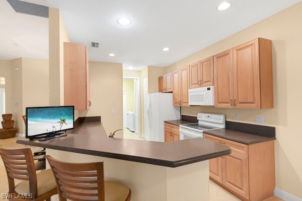 kitchen with white appliances, a breakfast bar, built in desk, kitchen peninsula, and light brown cabinets