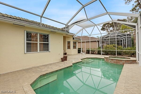 view of pool with an in ground hot tub, a patio, and glass enclosure