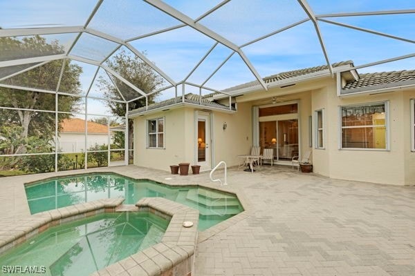 back of property with a swimming pool with hot tub, a patio, and glass enclosure