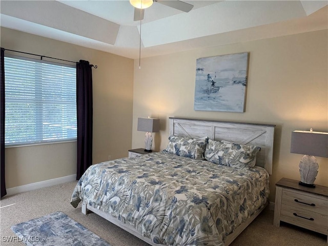 bedroom featuring ceiling fan, a tray ceiling, and light carpet