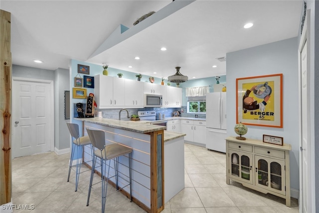 kitchen with a kitchen bar, white cabinetry, kitchen peninsula, white appliances, and decorative backsplash