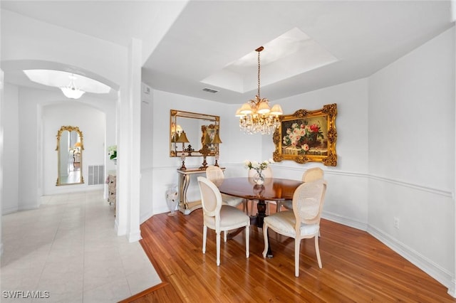 dining area featuring a notable chandelier, light hardwood / wood-style floors, and a raised ceiling