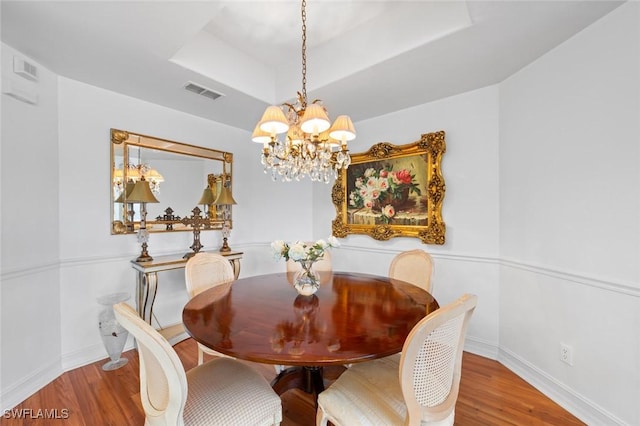 dining space with an inviting chandelier, hardwood / wood-style flooring, and a raised ceiling