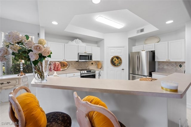 kitchen featuring white cabinetry, a kitchen breakfast bar, a raised ceiling, stainless steel appliances, and backsplash