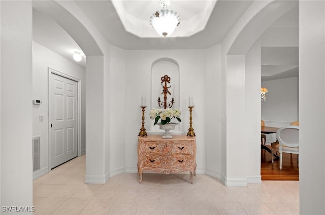 hall with light tile patterned flooring and a tray ceiling