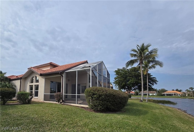 back of house featuring a water view, a lawn, and a lanai