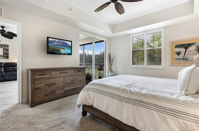 carpeted bedroom featuring ceiling fan, access to exterior, multiple windows, and a tray ceiling