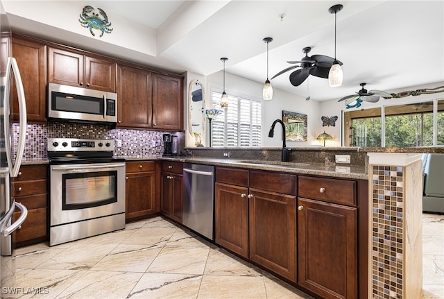 kitchen with appliances with stainless steel finishes, dark stone counters, sink, kitchen peninsula, and ceiling fan