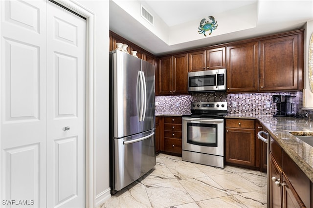 kitchen featuring dark brown cabinetry, appliances with stainless steel finishes, and dark stone countertops