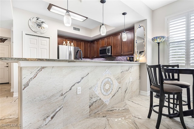 kitchen featuring backsplash, kitchen peninsula, hanging light fixtures, a kitchen breakfast bar, and stainless steel appliances