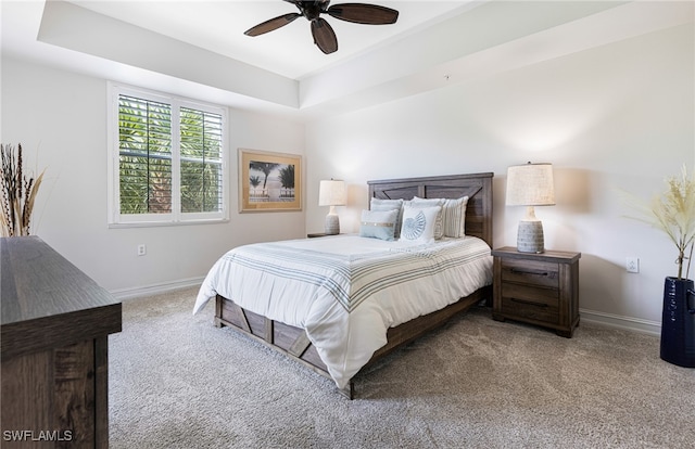 carpeted bedroom with ceiling fan and a raised ceiling