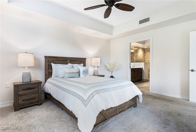 bedroom featuring ceiling fan, light carpet, a raised ceiling, and ensuite bath