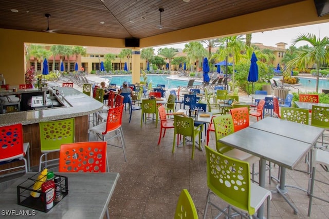 view of patio featuring ceiling fan, a bar, and a community pool