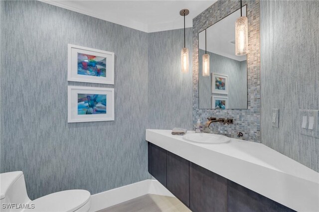 bathroom featuring toilet, ornamental molding, and vanity