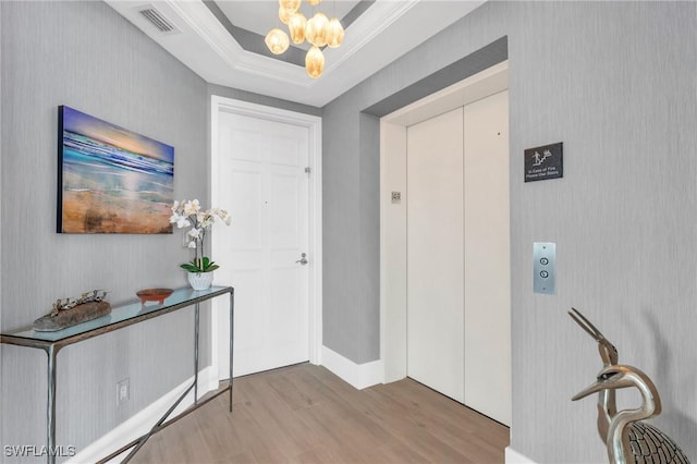 foyer entrance with visible vents, ornamental molding, wood finished floors, elevator, and a chandelier
