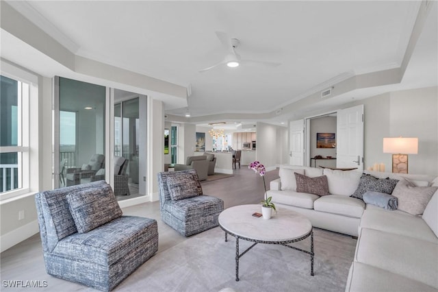 living area featuring a raised ceiling, ceiling fan with notable chandelier, light wood-style flooring, and visible vents