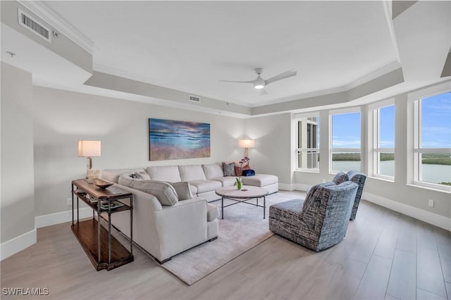 living room with ornamental molding, a raised ceiling, a water view, and light hardwood / wood-style flooring