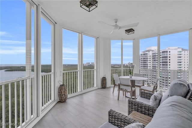 sunroom with a water view, plenty of natural light, expansive windows, and wood finished floors