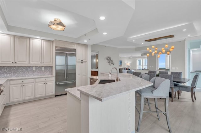 kitchen with light wood-style floors, a kitchen breakfast bar, a tray ceiling, built in fridge, and a sink