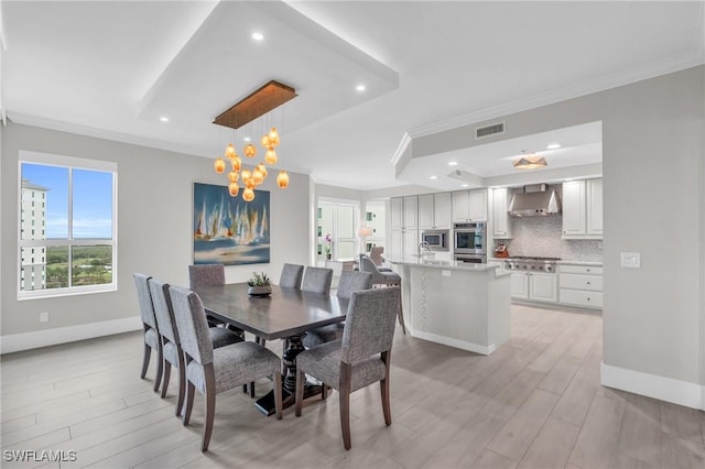 dining space with ornamental molding, light hardwood / wood-style floors, a tray ceiling, and sink