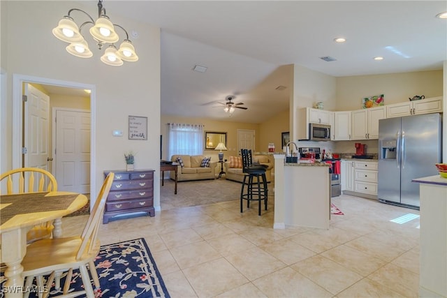 kitchen with a breakfast bar area, light stone counters, hanging light fixtures, stainless steel appliances, and white cabinets