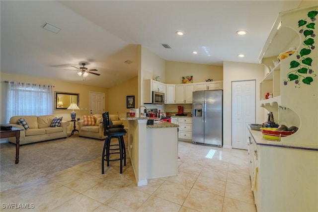 kitchen featuring vaulted ceiling, light tile patterned flooring, white cabinetry, a kitchen bar, and stainless steel appliances