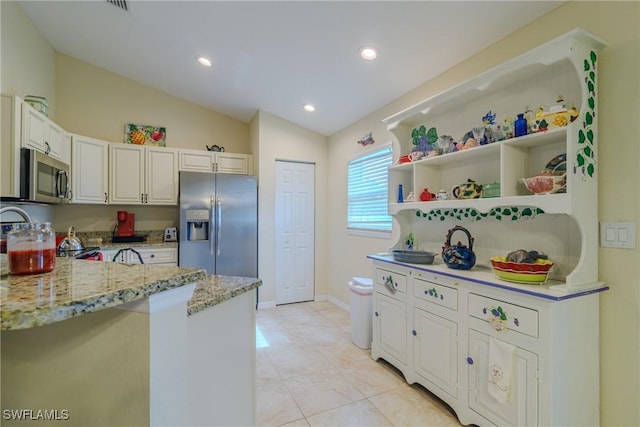 kitchen featuring vaulted ceiling, white cabinets, kitchen peninsula, stainless steel appliances, and light stone countertops