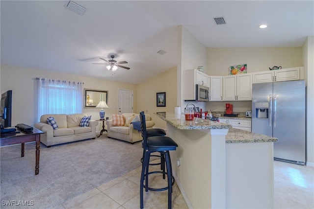 kitchen with a breakfast bar area, appliances with stainless steel finishes, white cabinetry, vaulted ceiling, and kitchen peninsula