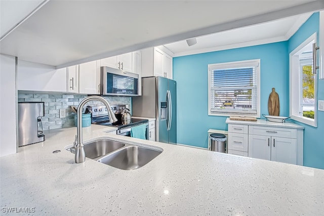 kitchen featuring light stone counters, tasteful backsplash, appliances with stainless steel finishes, white cabinets, and a sink