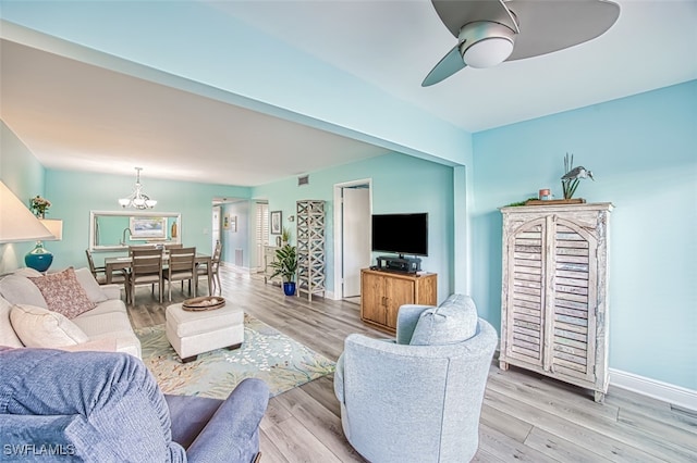 living area featuring ceiling fan with notable chandelier, light wood finished floors, visible vents, and baseboards