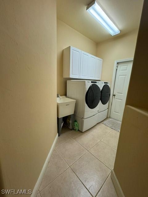 clothes washing area with cabinets, light tile patterned floors, washer and clothes dryer, and sink