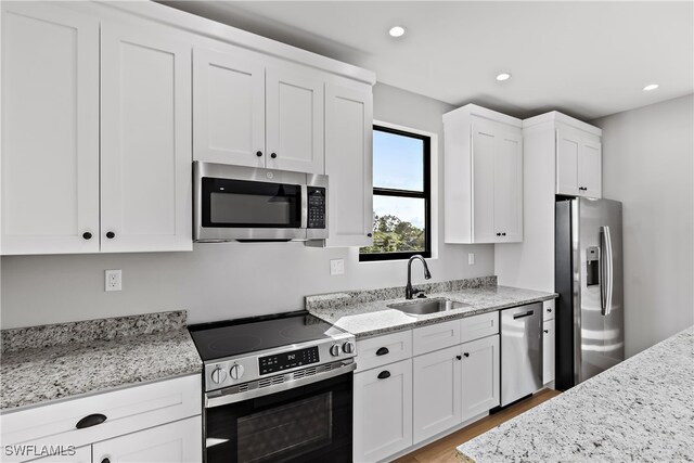 kitchen with light stone countertops, white cabinets, stainless steel appliances, light hardwood / wood-style floors, and sink