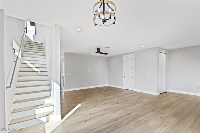 unfurnished living room with ceiling fan with notable chandelier and light wood-type flooring