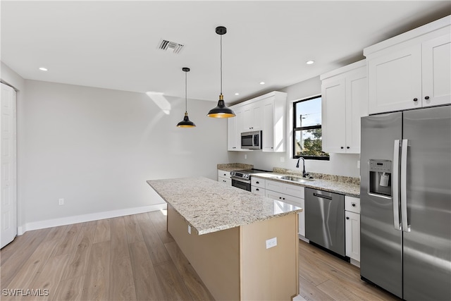 kitchen with appliances with stainless steel finishes, a kitchen island, decorative light fixtures, white cabinetry, and sink